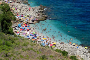 Photo of a beach scene with brightly coloured umbrellas on a beach in Zingaro nature reserve in Sicily.
