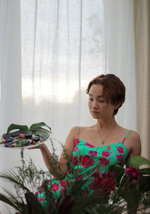 Model wearing Crimson Rose midi slip dress with green, red, pink floral print from the Island Dreams collection holding a plate with purple potatoes with feta and beetroot whip and pea, pistachio and mint pesto, garnished with pansies. Photography 0K.