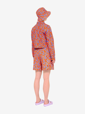 Model facing away from us wearing Crimson Rose cropped cotton drill jacket and bucket hat with orange and blue floral print and lilac sandals. Photography Rowan Corr.
