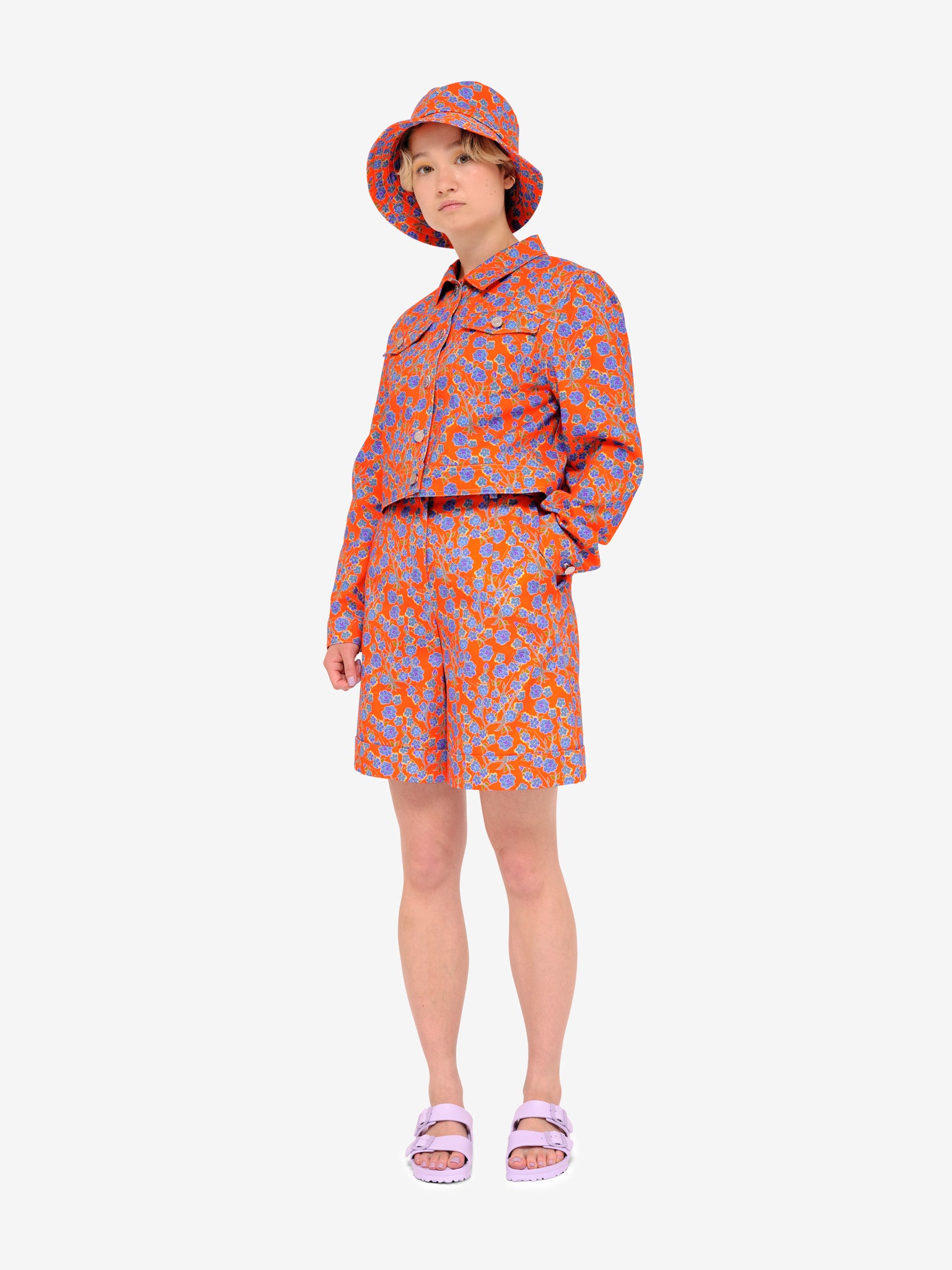 Model wearing Crimson Rose cropped cotton drill jacket and bucket hat with orange and blue floral print and lilac sandals. Photography Rowan Corr.