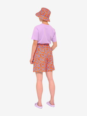 Model facing away from us wearing Crimson Rose cotton drill culottes and bucket hat with orange and blue floral print, lilac Es Vedrà T-shirt and lilac sandals. Photography Rowan Corr.